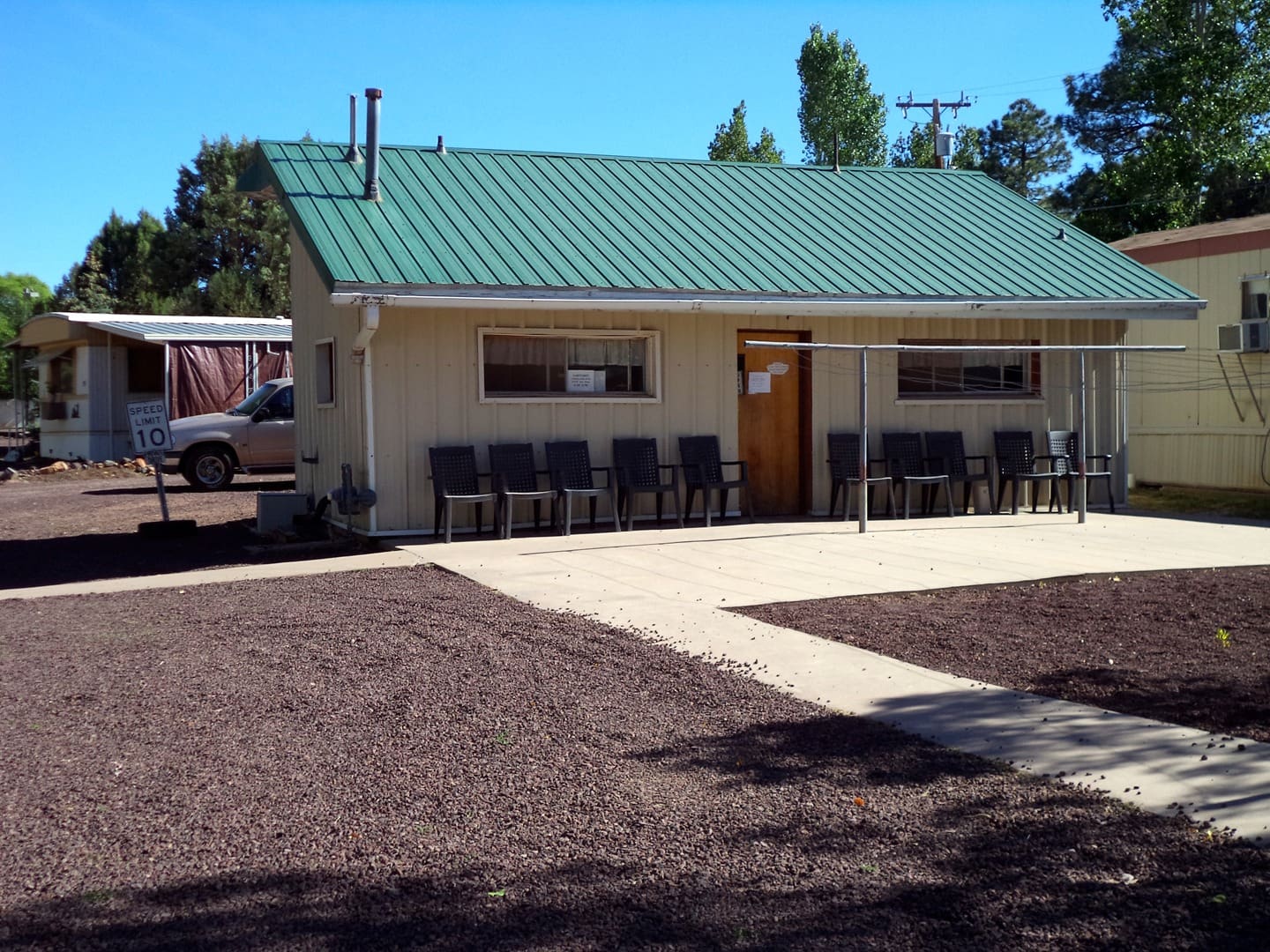 A small white building with green roof and chairs in front of it.